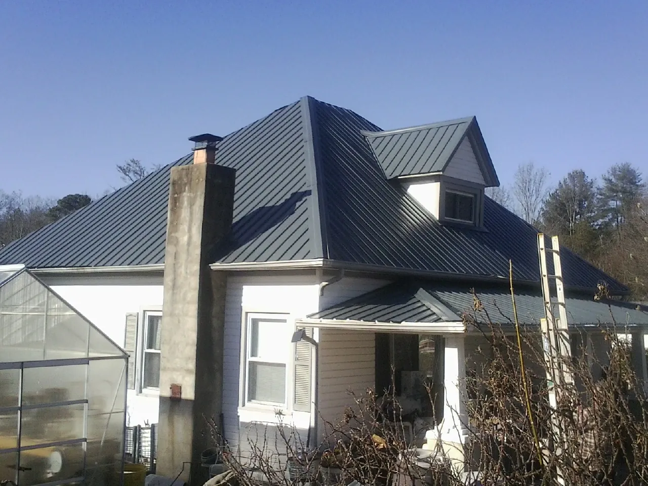 Dark blue standing seam metal roof on a white farmhouse with dormer — Slate & Tile Roof Repair by Roofing Brothers in Crivitz
