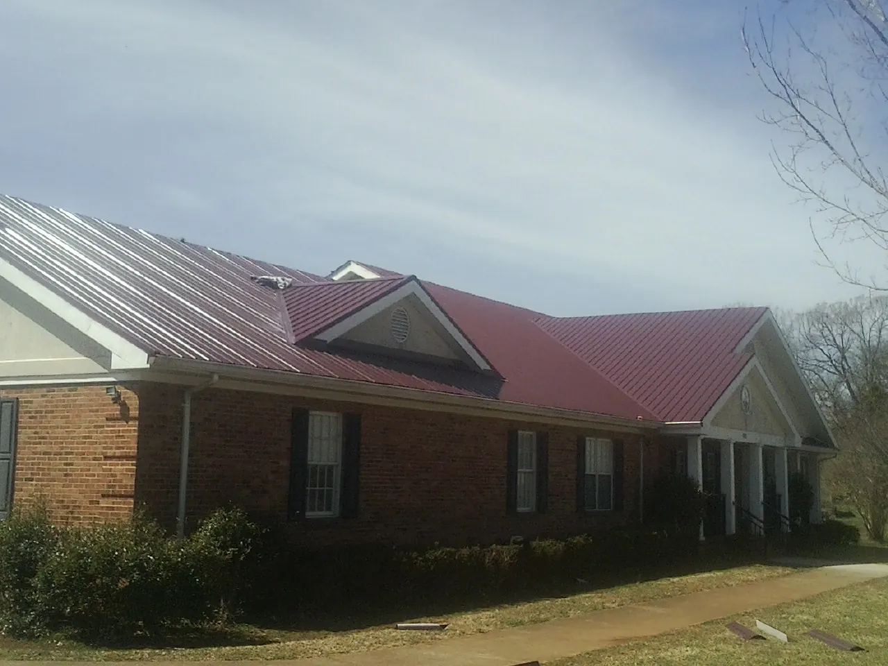 Red metal roof with gabled entries on a long brick building, from a Hail Damage Roof Repair job in Crivitz