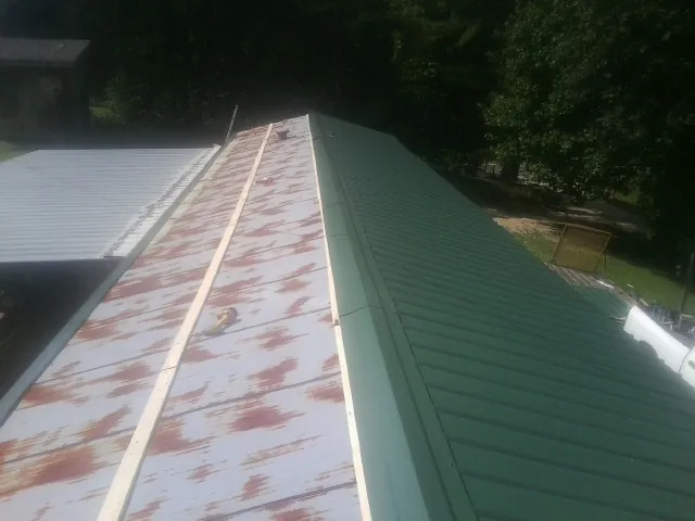 Old rusted panels beside newly installed green metal roofing — Wind Damage Roof Repair by Roofing Brothers in Crivitz