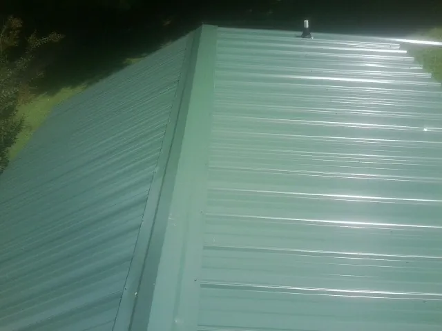 New green metal panels meeting at the ridge of a roof — Flat Roof Repair work by our crew in Crivitz