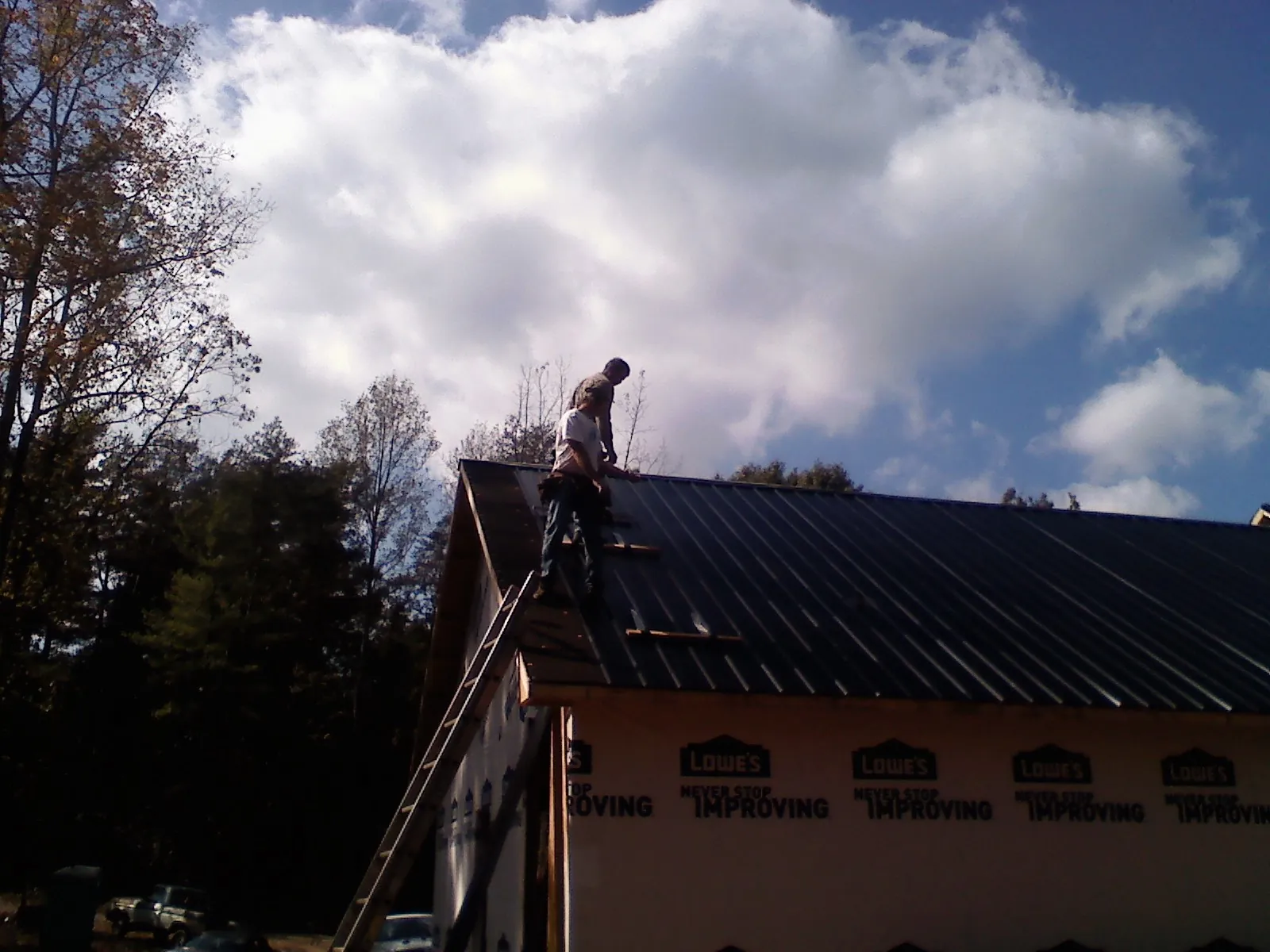 Roofer fastening dark metal panels high against a cloudy sky, from a Roof Inspection job in Crivitz