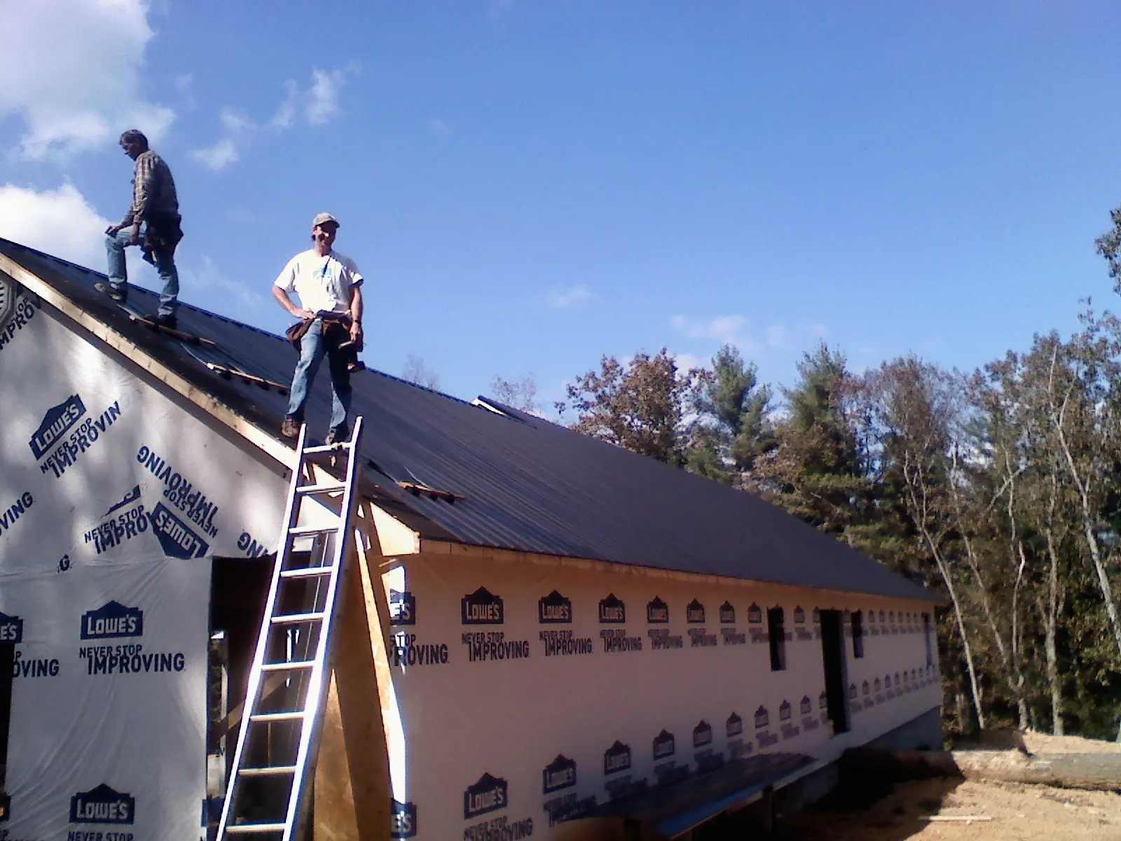 Two roofers standing on a long dark metal roof over a wrapped building in Crivitz