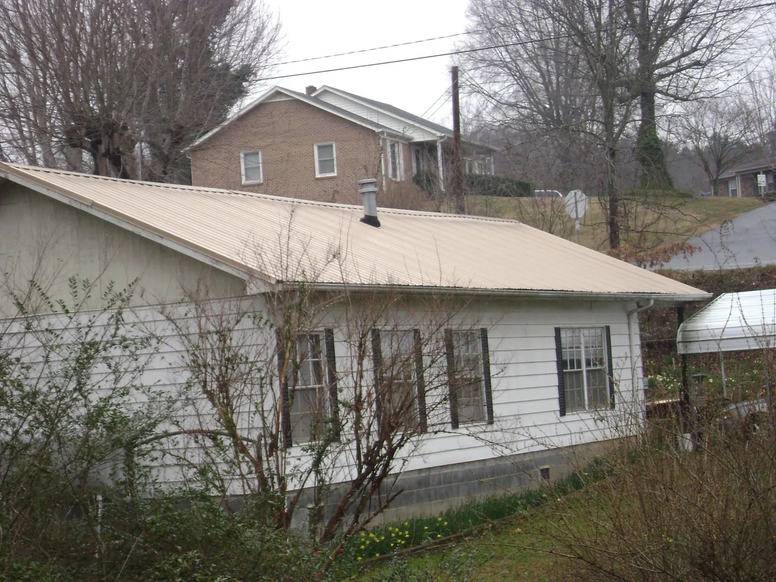Tan metal roof on a white sided house set into a hillside — Commercial Roofing by Roofing Brothers in Crivitz